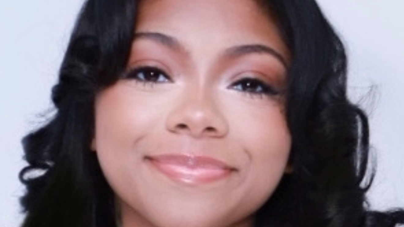 Woman with long, wavy hair wearing a black top against a light gray background