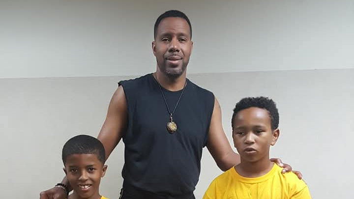 Man with three children wearing matching yellow 'Old School vs New School' t-shirts indoors.